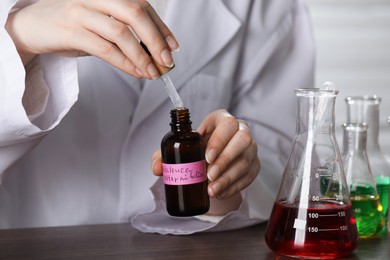Photo of Professional perfumer developing luxury perfume at wooden table in laboratory, closeup