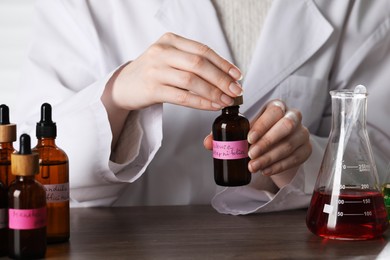 Photo of Professional perfumer developing luxury perfume at wooden table in laboratory, closeup