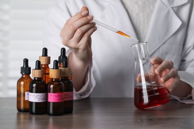 Photo of Professional perfumer developing luxury perfume at wooden table in laboratory, closeup