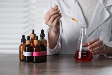 Photo of Professional perfumer developing luxury perfume at wooden table in laboratory, closeup