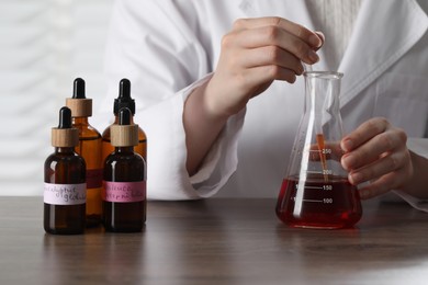 Photo of Professional perfumer developing luxury perfume at wooden table in laboratory, closeup