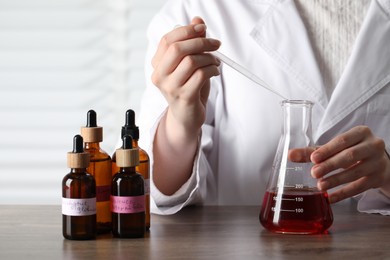 Photo of Professional perfumer developing luxury perfume at wooden table in laboratory, closeup