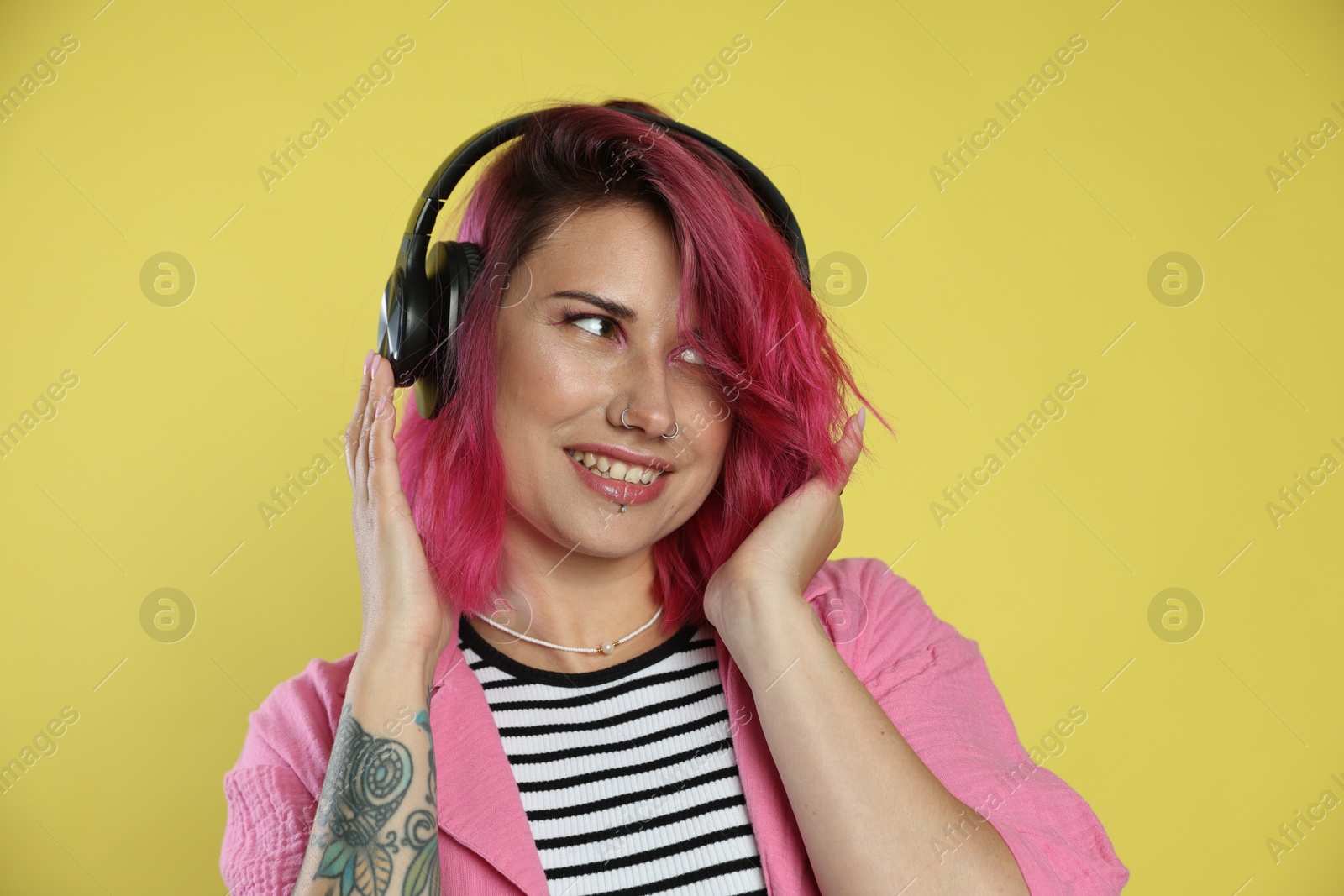 Beautiful woman with pink dyed hair listening to music on yellow background Photo of Beautiful woman with pink dyed hair listening to music on yellow background