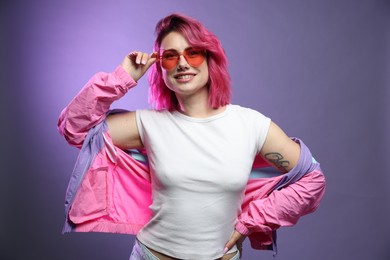 Photo of Beautiful woman with pink dyed hair in sunglasses on violet gradient background