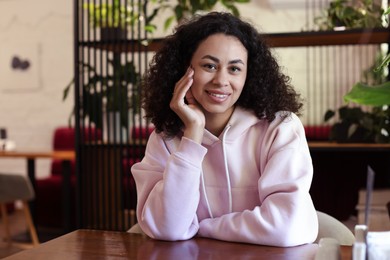Photo of Portrait of smiling Latin American woman at table in cafe
