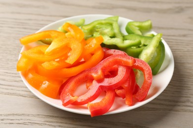 Photo of Slices of fresh colorful bell peppers on wooden table, closeup