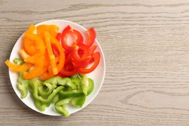 Photo of Slices of fresh colorful bell peppers on wooden table, top view. Space for text