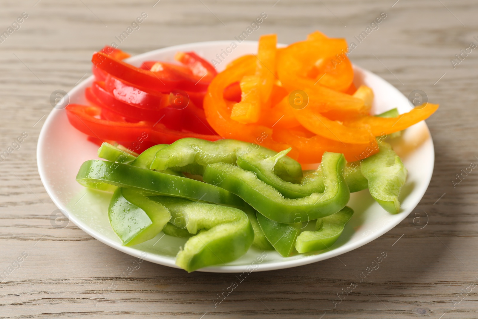 Photo of Slices of fresh colorful bell peppers on wooden table, closeup