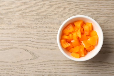 Photo of Pieces of fresh orange bell pepper in bowl on wooden table, top view. Space for text
