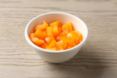 Photo of Pieces of fresh orange bell pepper in bowl on wooden table, closeup