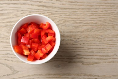 Photo of Pieces of fresh red bell pepper in bowl on wooden table, top view. Space for text