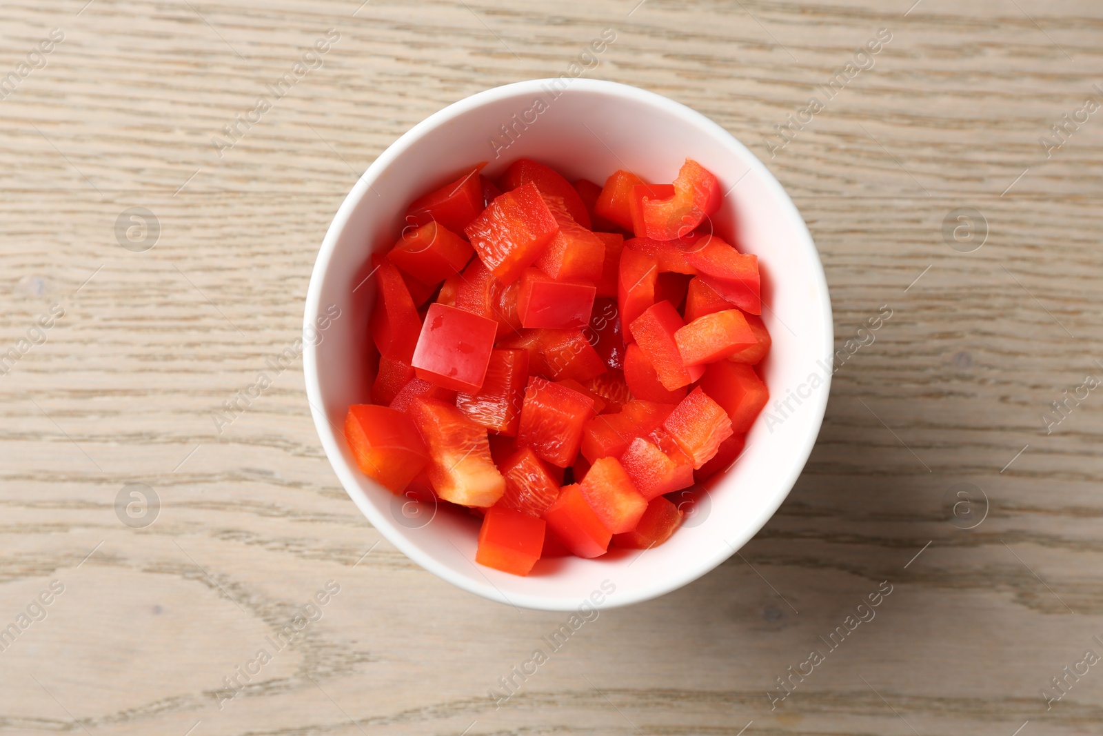 Photo of Pieces of fresh red bell pepper in bowl on wooden table, top view