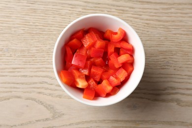Photo of Pieces of fresh red bell pepper in bowl on wooden table, top view
