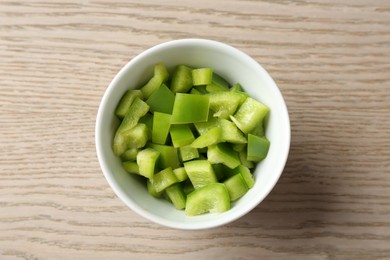 Photo of Pieces of fresh green bell pepper in bowl on wooden table, top view