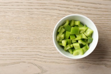 Photo of Pieces of fresh green bell pepper in bowl on wooden table, top view. Space for text