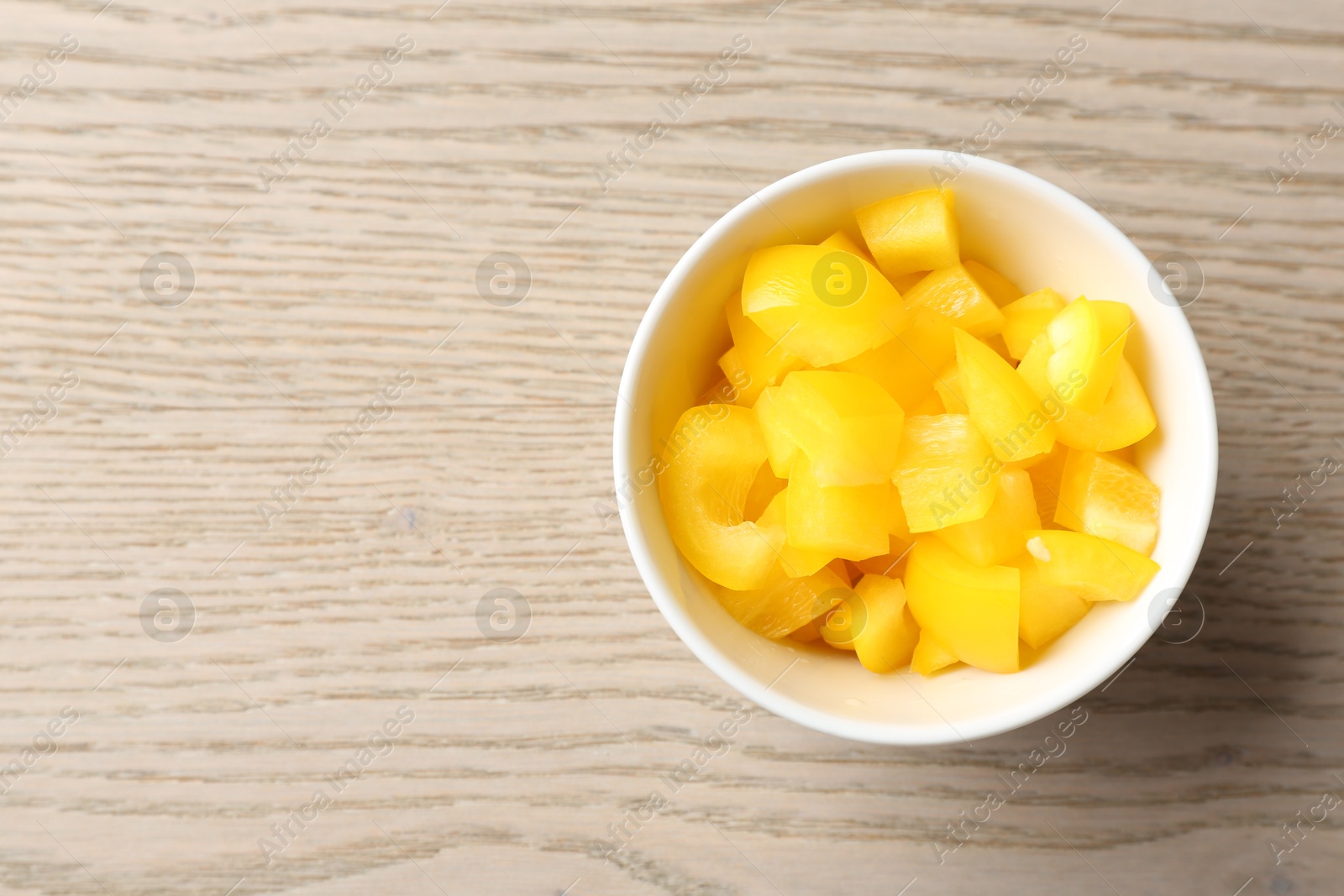 Photo of Pieces of fresh yellow bell pepper in bowl on wooden table, top view. Space for text