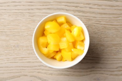 Photo of Pieces of fresh yellow bell pepper in bowl on wooden table, top view