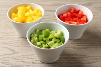 Photo of Pieces of fresh colorful bell peppers in bowls on wooden table, closeup