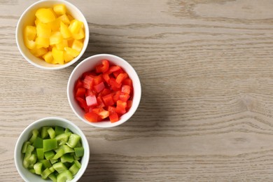 Photo of Pieces of fresh colorful bell peppers in bowls on wooden table, flat lay. Space for text
