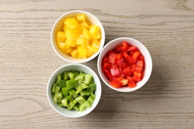 Photo of Pieces of fresh colorful bell peppers in bowls on wooden table, flat lay