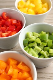 Photo of Pieces of fresh colorful bell peppers in bowls on wooden table, closeup