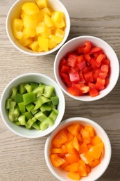 Photo of Pieces of fresh colorful bell peppers in bowls on wooden table, flat lay
