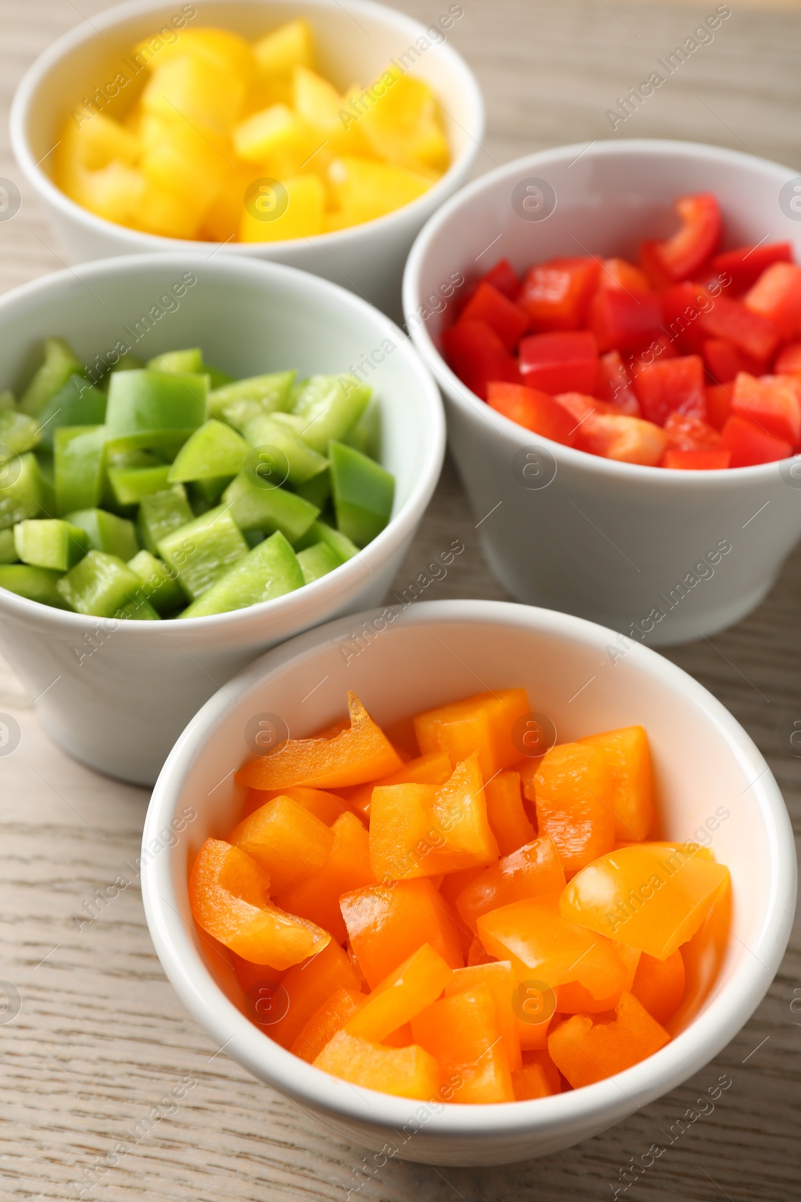Pieces of fresh colorful bell peppers in bowls on wooden table, closeup Photo of Pieces of fresh colorful bell peppers in bowls on wooden table, closeup
