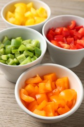 Photo of Pieces of fresh colorful bell peppers in bowls on wooden table, closeup