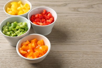Photo of Pieces of fresh colorful bell peppers in bowls on wooden table, closeup. Space for text