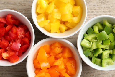 Photo of Pieces of fresh colorful bell peppers in bowls on wooden table, flat lay