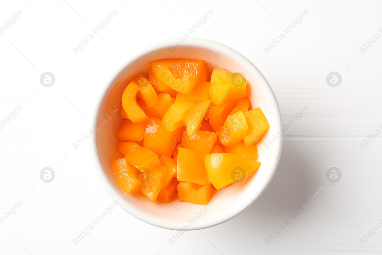 Photo of Pieces of fresh orange bell pepper in bowl on white wooden table, top view