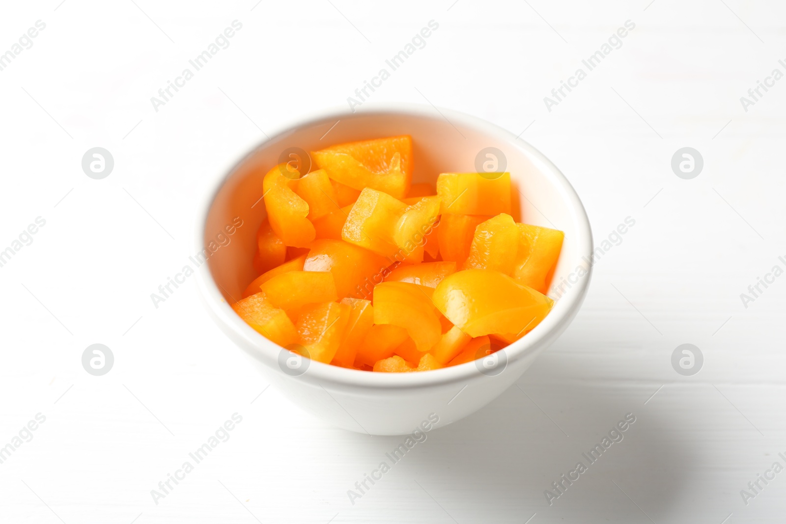 Photo of Pieces of fresh orange bell pepper in bowl on white wooden table, closeup