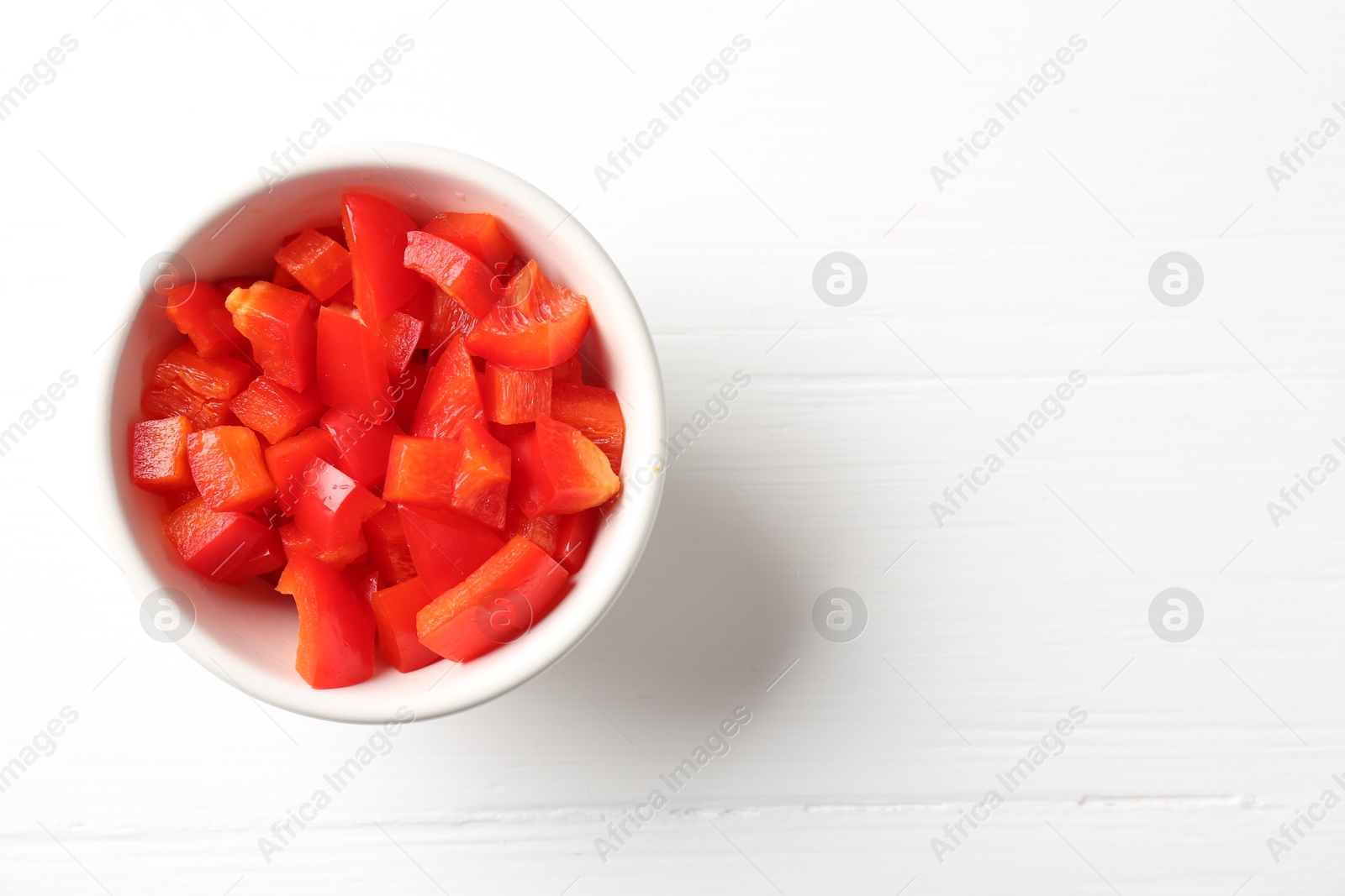 Photo of Pieces of fresh red bell pepper in bowl on white wooden table, top view. Space for text