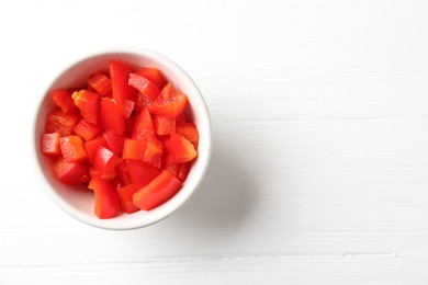 Photo of Pieces of fresh red bell pepper in bowl on white wooden table, top view. Space for text