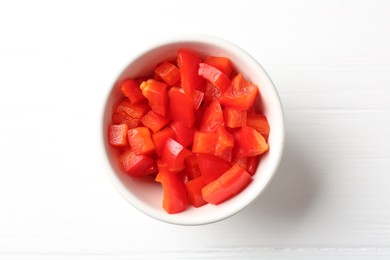 Photo of Pieces of fresh red bell pepper in bowl on white wooden table, top view