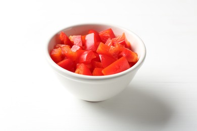 Photo of Pieces of fresh red bell pepper in bowl on white wooden table, closeup