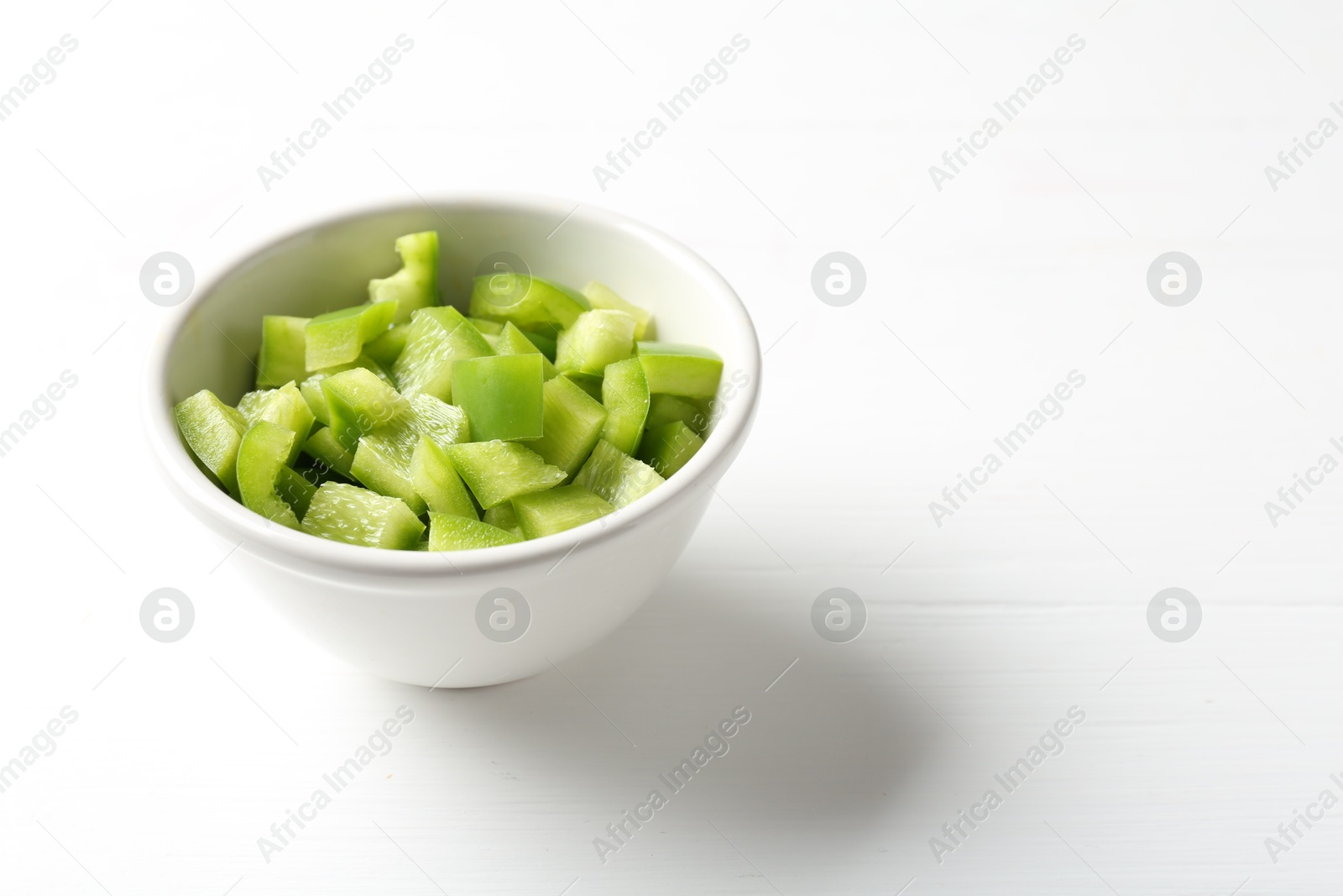 Photo of Pieces of fresh green bell pepper in bowl on white wooden table, closeup. Space for text