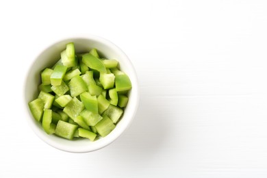 Photo of Pieces of fresh green bell pepper in bowl on white wooden table, top view. Space for text