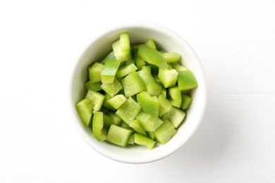Photo of Pieces of fresh green bell pepper in bowl on white wooden table, top view