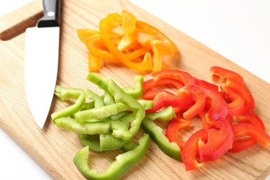 Photo of Slices of fresh colorful bell peppers and knife on white table, closeup