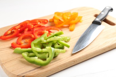 Photo of Slices of fresh colorful bell peppers and knife on white wooden table, closeup