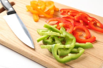 Photo of Slices of fresh colorful bell peppers and knife on white wooden table, closeup