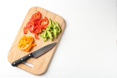 Photo of Slices of fresh colorful bell peppers and knife on white wooden table, top view. Space for text