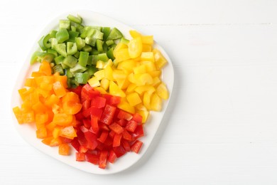 Photo of Pieces of fresh colorful bell peppers on white wooden table, top view. Space for text
