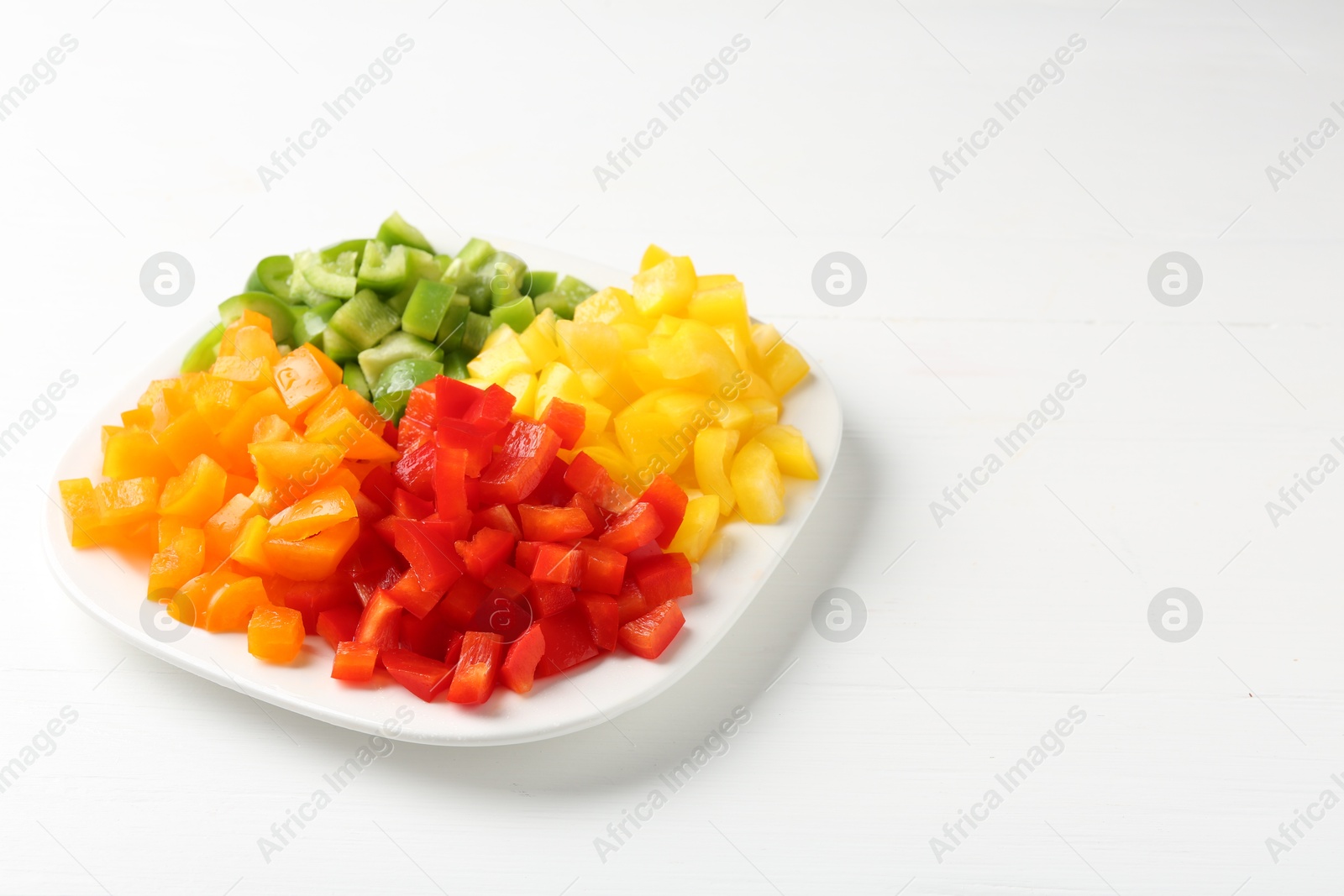 Photo of Pieces of fresh colorful bell peppers on white wooden table, closeup. Space for text