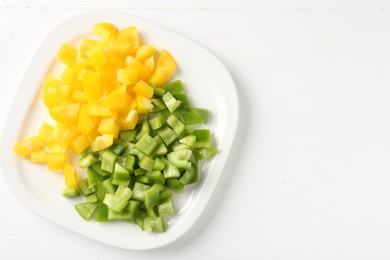 Photo of Pieces of fresh colorful bell peppers on white wooden table, top view. Space for text