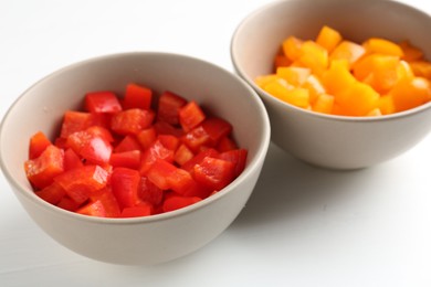 Photo of Pieces of fresh colorful bell peppers in bowls on white table, closeup
