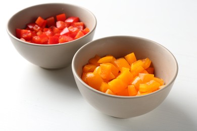 Photo of Pieces of fresh colorful bell peppers in bowls on white wooden table, closeup