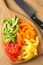 Photo of Slices of fresh colorful bell peppers and knife on wooden table, flat lay