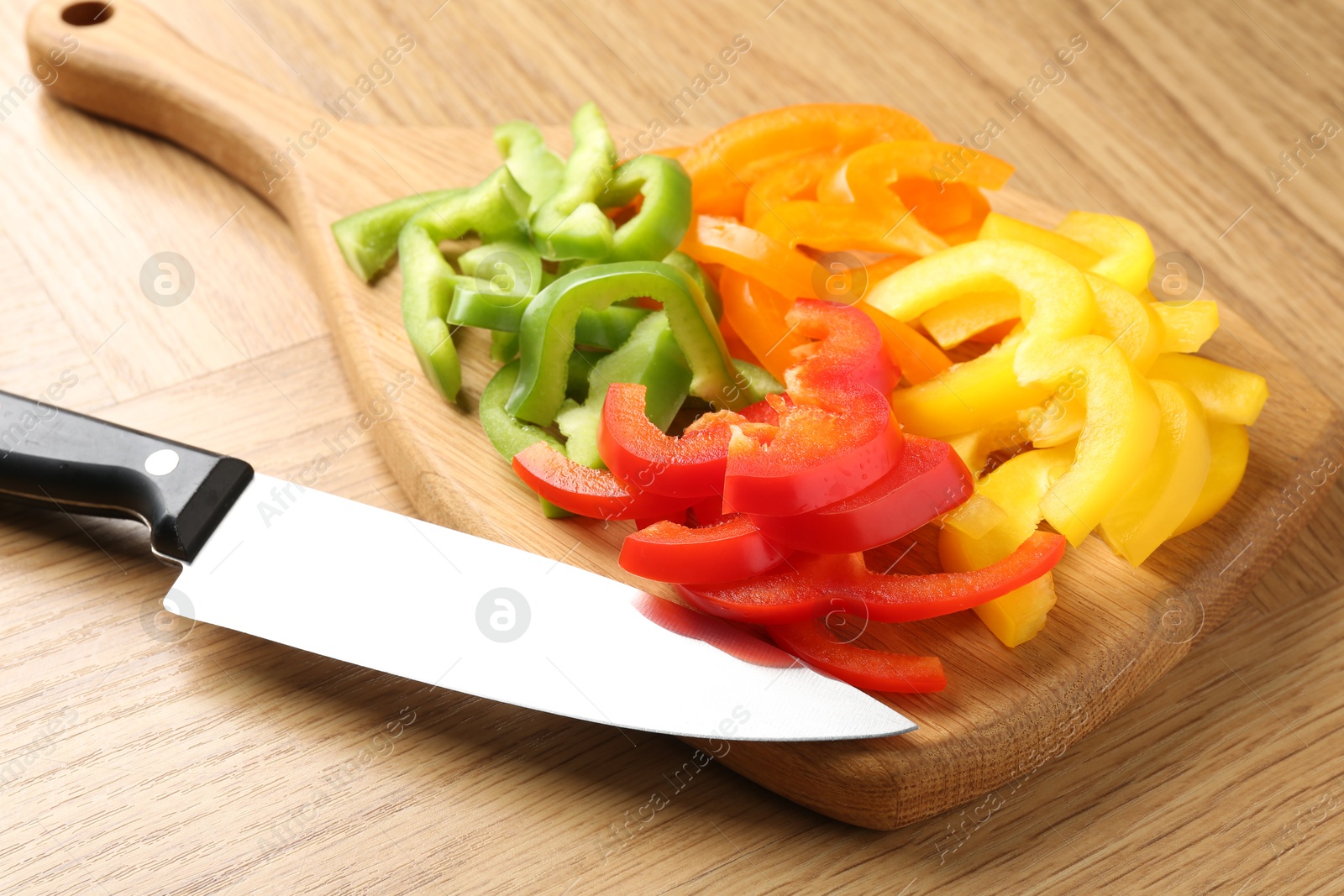 Slices of fresh colorful bell peppers and knife on wooden table, closeup Photo of Slices of fresh colorful bell peppers and knife on wooden table, closeup